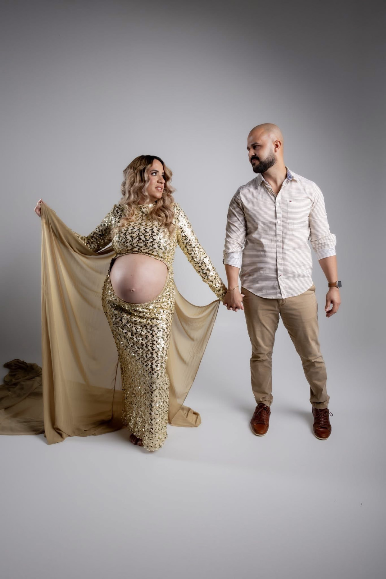 Pareja en sesión de maternidad con vestido dorado y tela beige